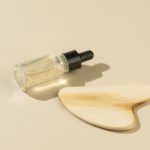 A dropper bottle with transparent antiaging serum with golden parts and a wooden gua sha massager