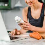Happy young woman searching info in laptop about food supplements in the kitchen